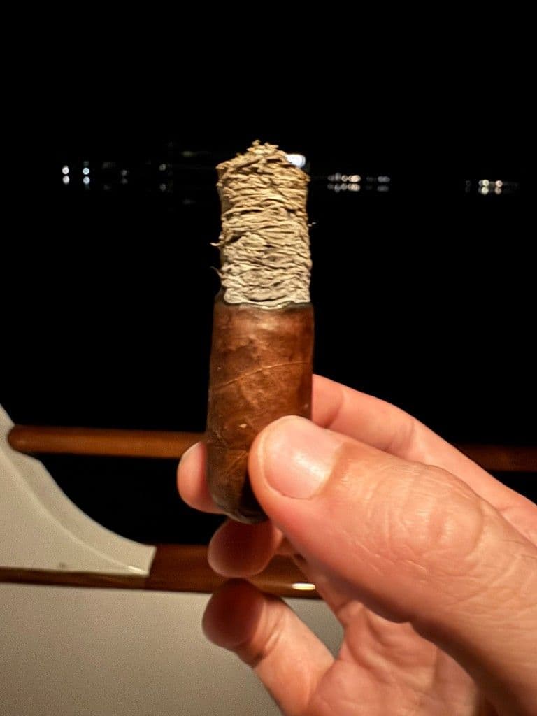 Late Hour Robusto with long layered ash held over a boat railing